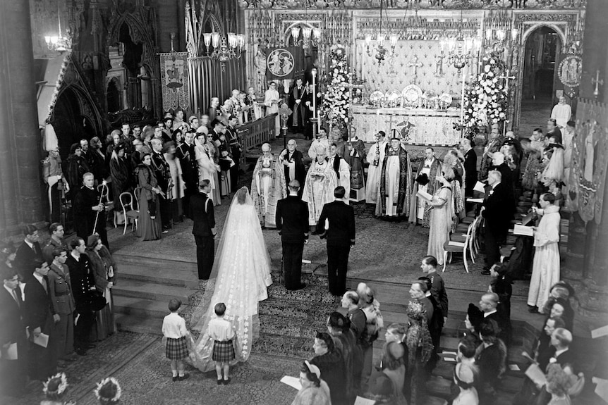 A black and white still of Princess Elizabeth and Philip at the altar of Westminster Abbey.