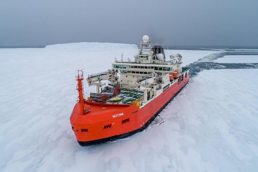 A bright red ship is seen from above breaking a path through sea ice