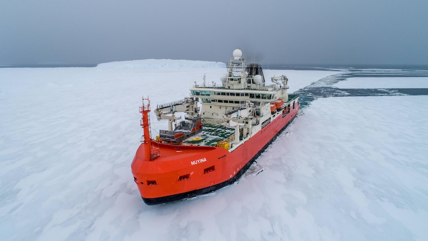 A bright red ship is seen from above breaking a path through sea ice