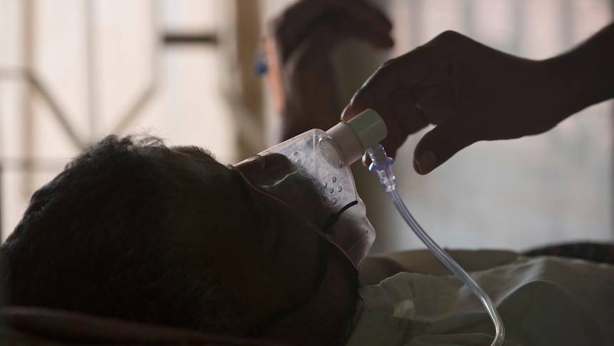 Someone adjusts the oxygen mask of a tuberculosis patient who is lying in a hospital bed 