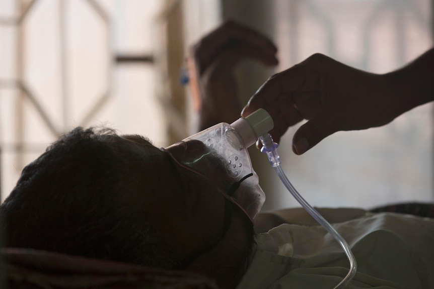 Someone adjusts the oxygen mask of a tuberculosis patient who is lying in a hospital bed 