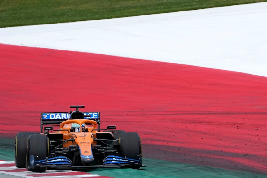 Daniel Ricciardo conduit sa voiture de F1 au bord de la piste près des couleurs du drapeau autrichien.