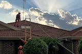 SES volunteers work to repair a roof that was damaged by a hailstorm.