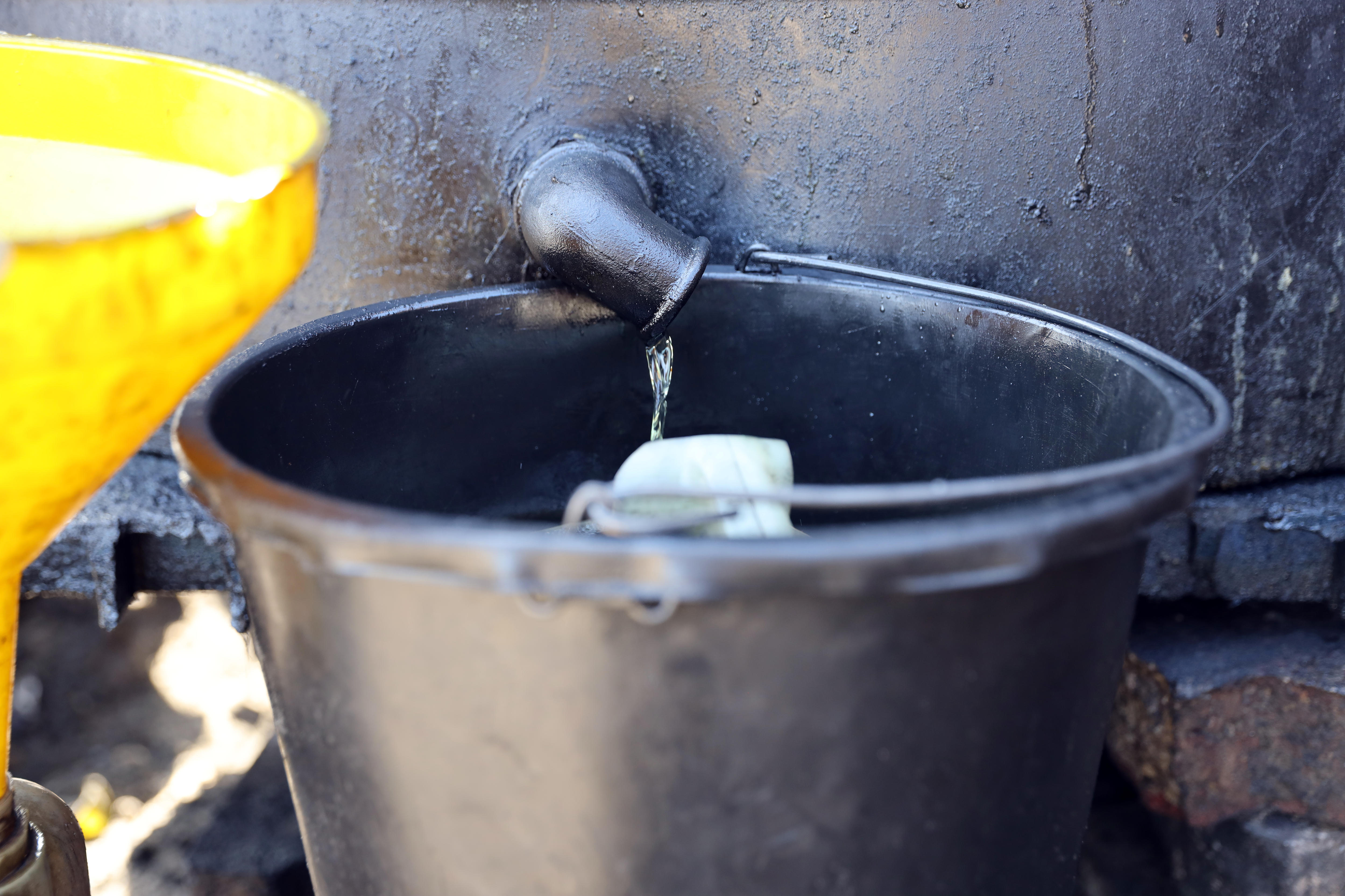 A low drip of oil out of a tap into a bucket.