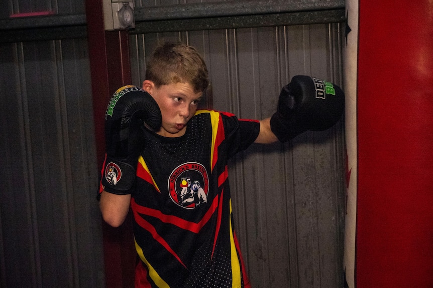 Young boy punching a boxing bag, with a look of determination on his face  