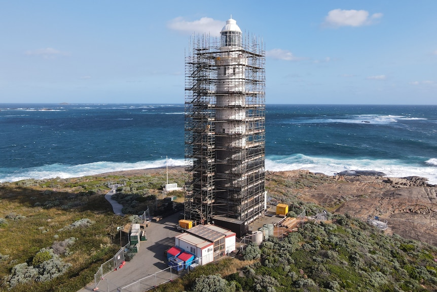 A lighthouse on a coastline covered in scaffolding works