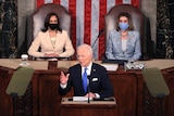 Kamala Harris wearing a white jacket and black mask and Nancy Pelosi wearing a grey jacket and blue mask look at Joe Biden.