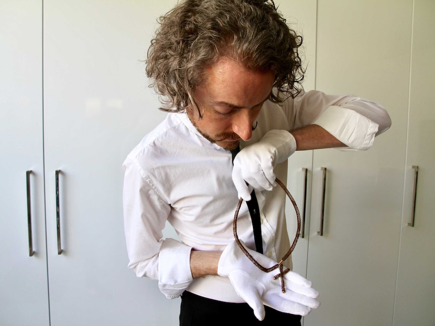 A man, wearing white gloves, holds a necklace and crucifix made from human hair