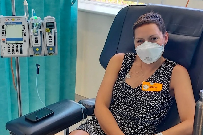 Young woman sits in medical chair with mask on connected to IV.