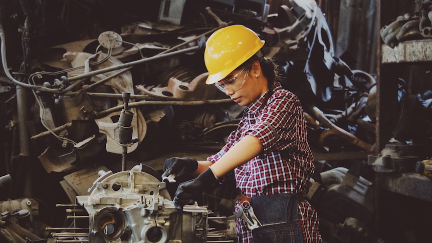 woman-wears-yellow-hard-hat-holding-vehicle-part