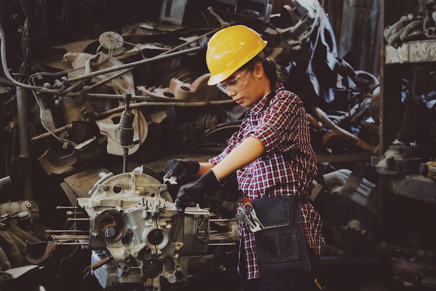 woman-wears-yellow-hard-hat-holding-vehicle-part