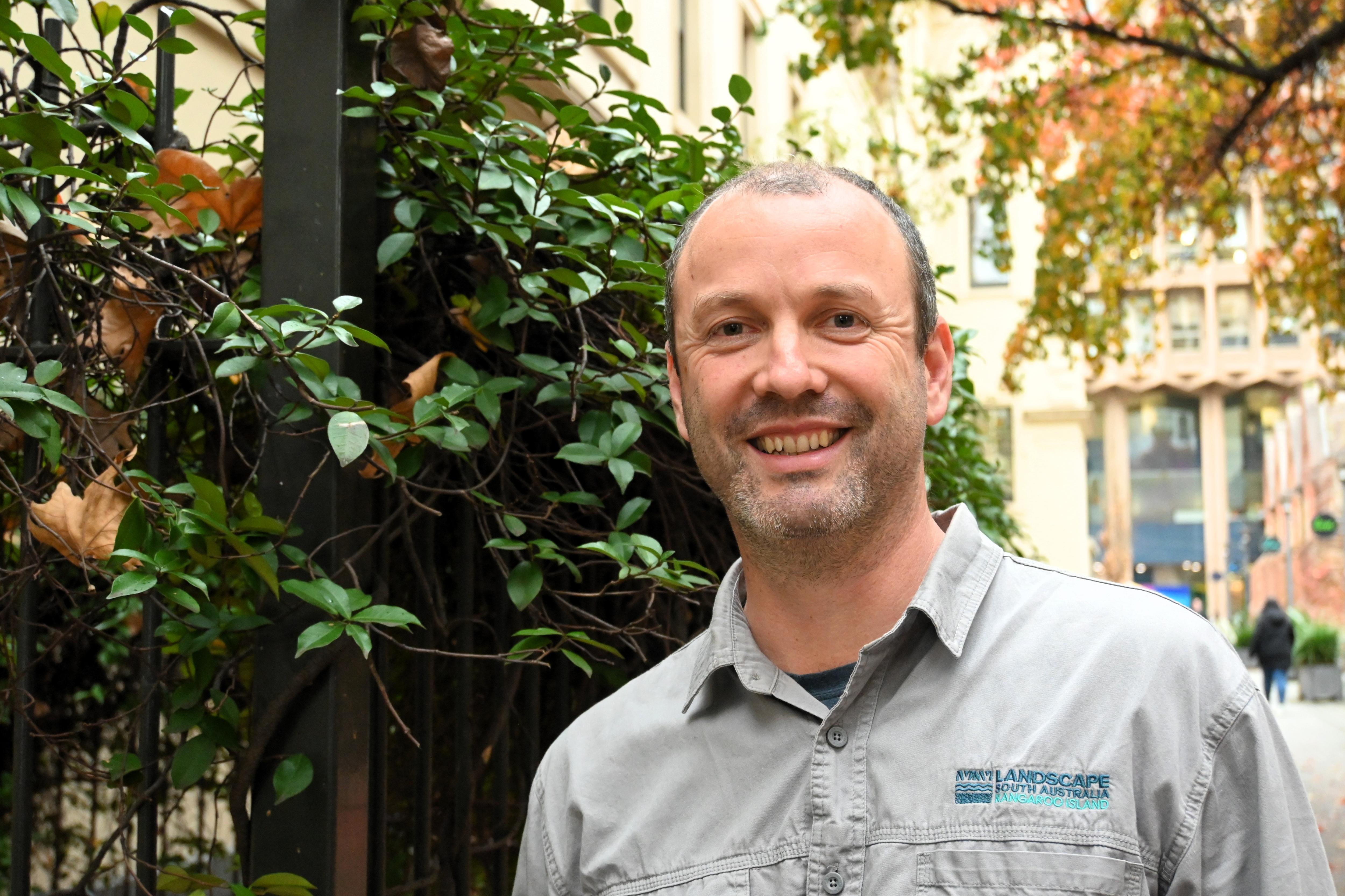 A man stands next to a bush in a shirt branded with the Kangaroo Island Landscape Board logo