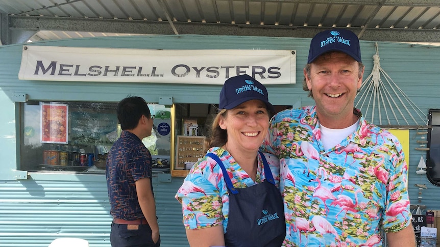 two people hold a tray of oysters in front of a caravan shop