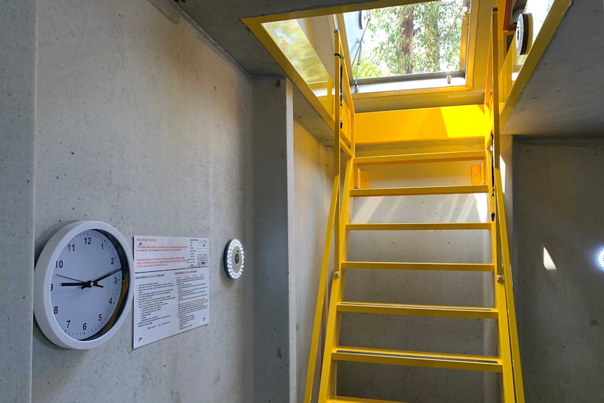 Yellow stairs down to a cement fire bunker, which has a clock on the wall.