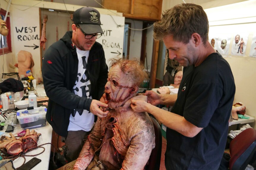 An actor in a gory costume while special effects crew remove his mask.