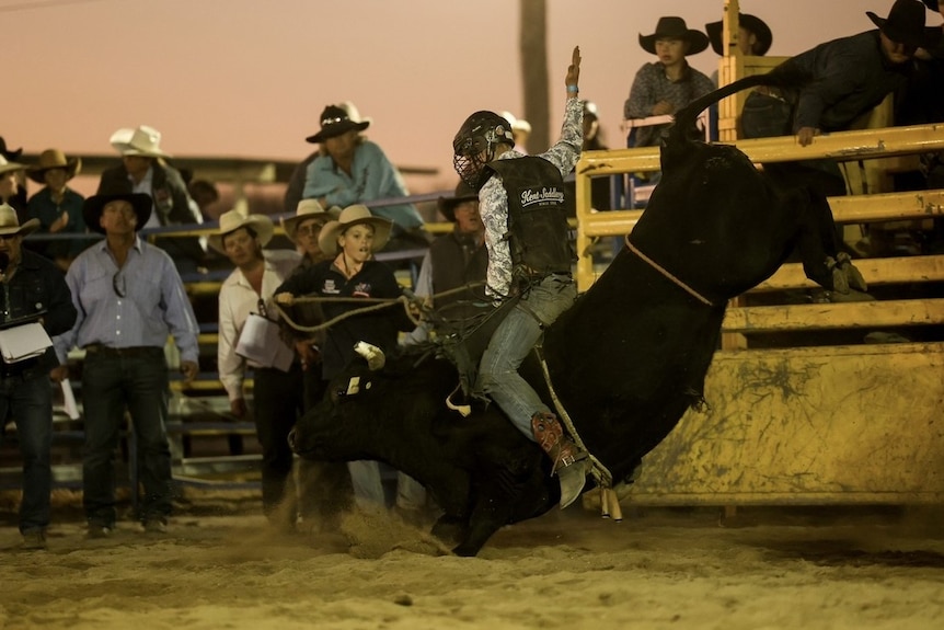 young man riding a bucking bull at a rodeo in front of spectators
