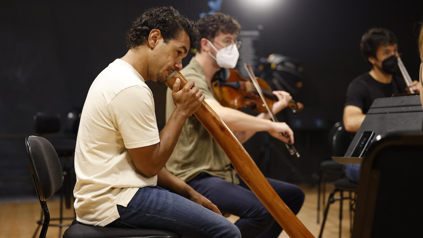 A man plays the didgeridoo next to a man playing a violin.