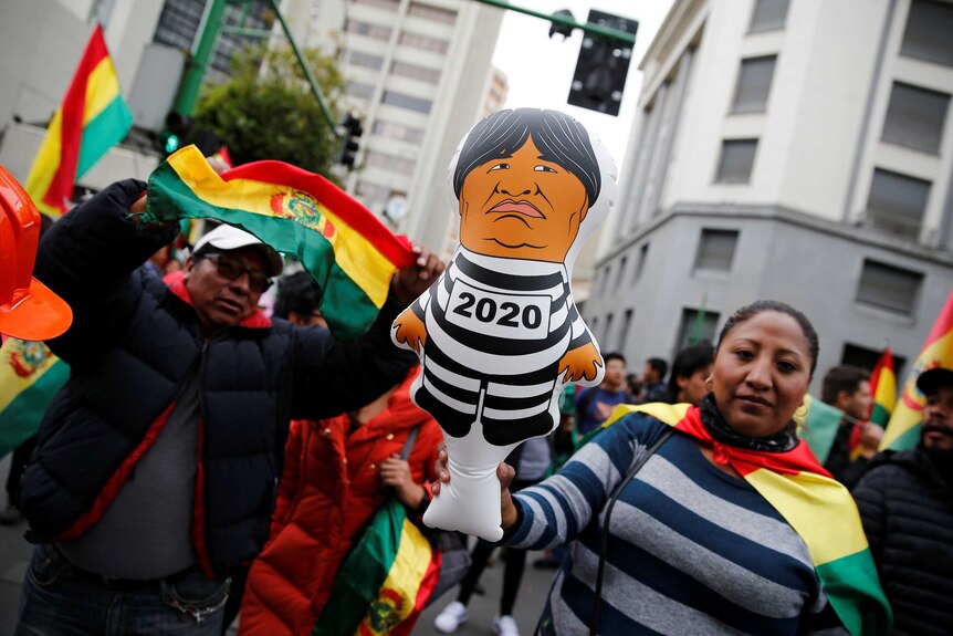 A woman holds a balloon resembling Bolivian President Evo Morales at a protest with Bolivian flags in the background