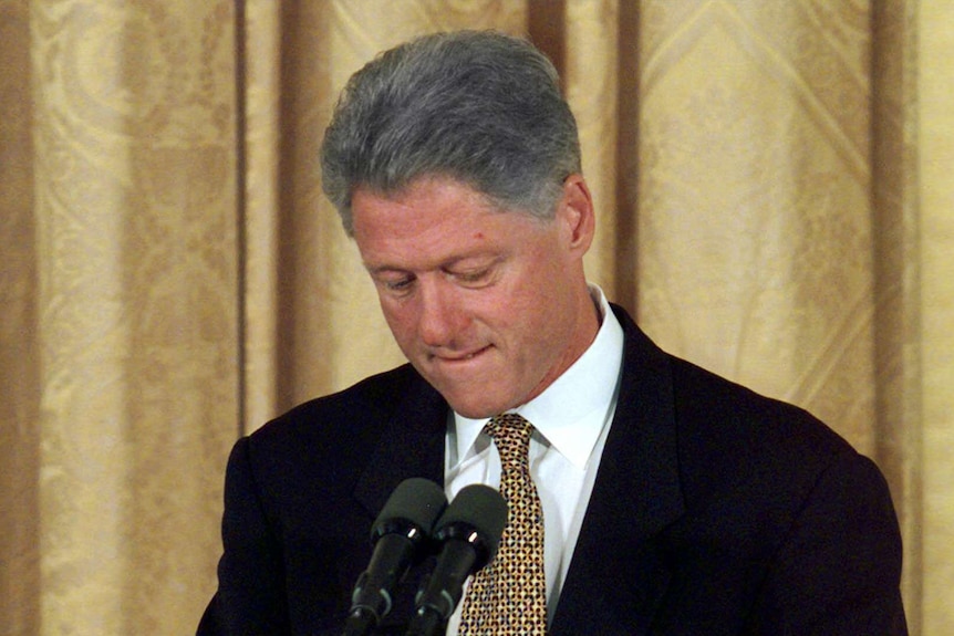 Bill Clinton stands at a lectern and looks towards the ground