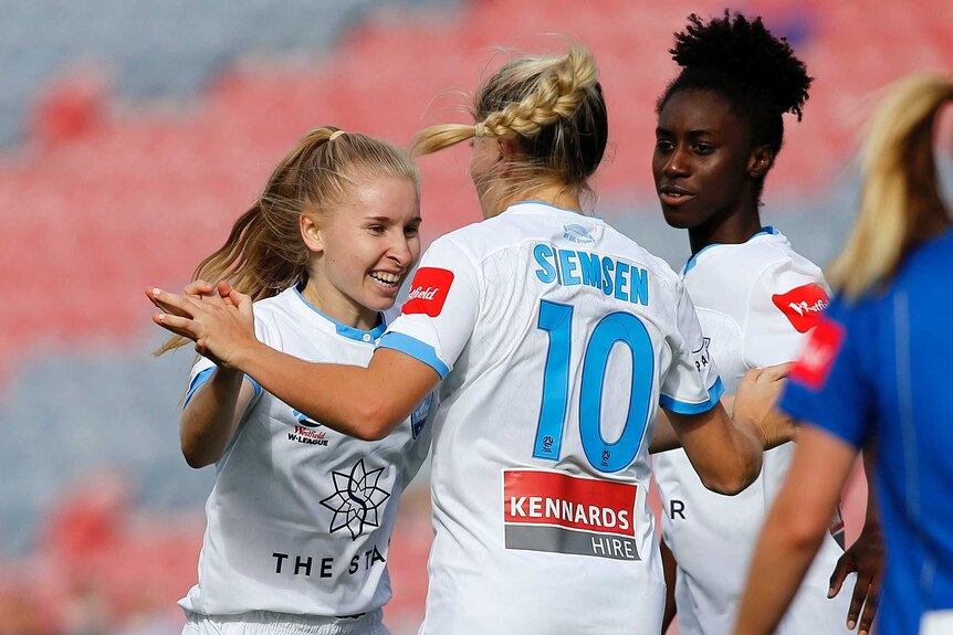 A female football player smiles and celebrates with her team after scoring a goal.