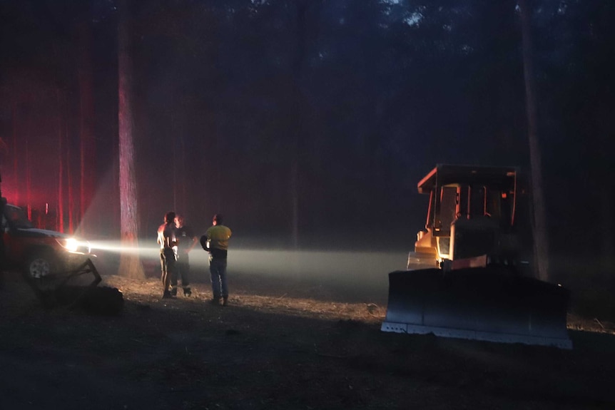 Firefighters stand lit up by the headlights.