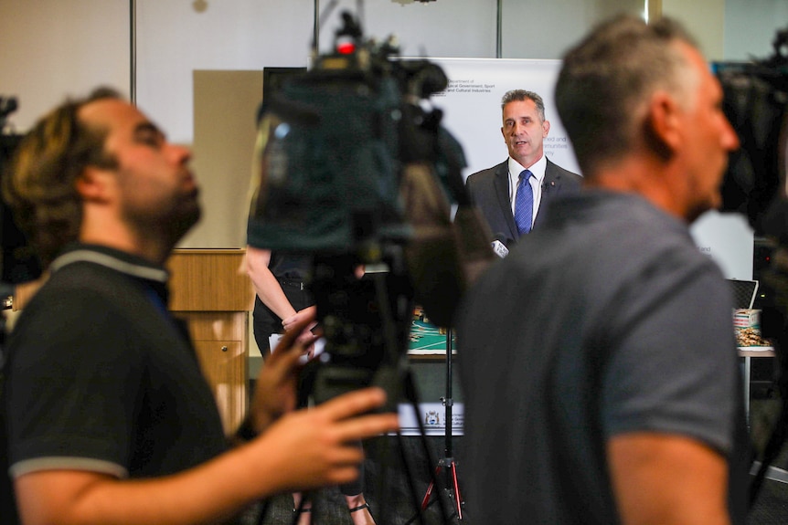 Paul Papalia is framed by camera equipment at a press conference