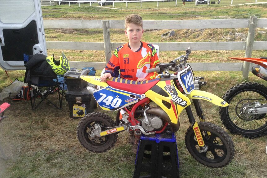 Young boy standing next to a motorbike at a motocross competition