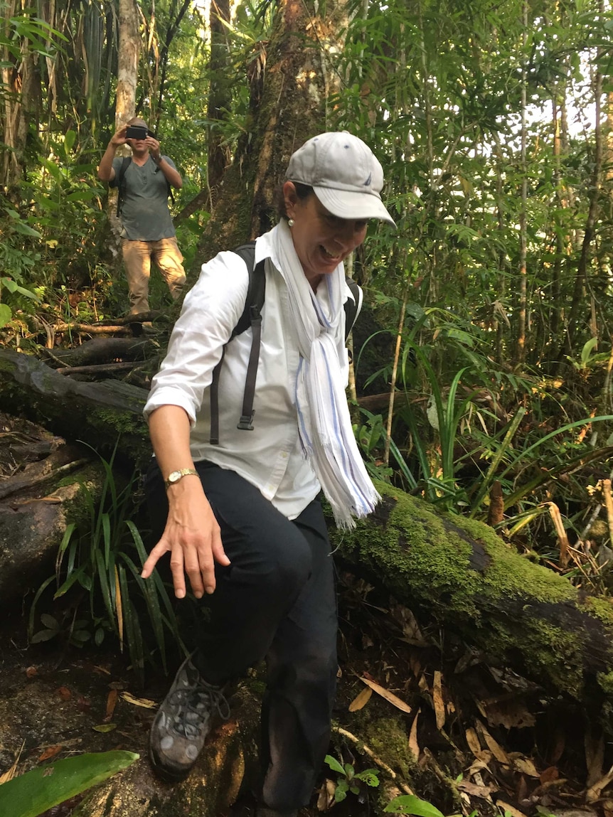 Reed stepping over large log across track in dense jungle.