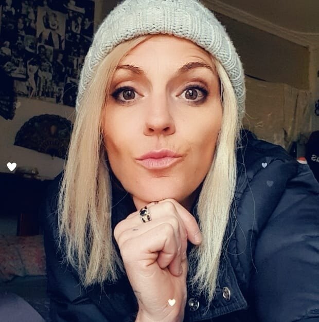 Blonde woman wearing sunglasses closed mouth smiles at camera