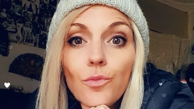 A blonde, dark-eyed woman in a beanie with a quizzical expression on her face.
