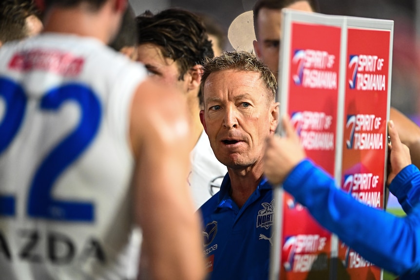 An AFL coach looks at a magnet board as he speaks to players at quarter-time during a match.