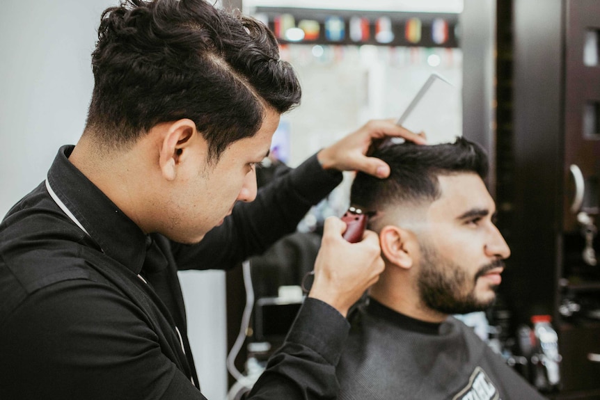 A man with short, dark hair shaving the sides of another man's head