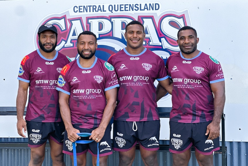Four men from Papua New Guinea wearing maroon training shirts standing in front of sign that reads Central Queensland Capras