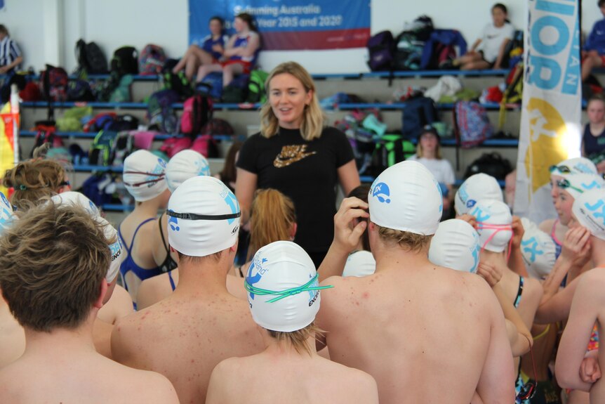 Olympic swimmer Ariarne Titmus speaks to a crowd of youths wearing swimming outfits. 