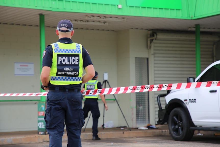 Several police officers standing by part of a shopping centre carpark sealed off with crime scene tape.