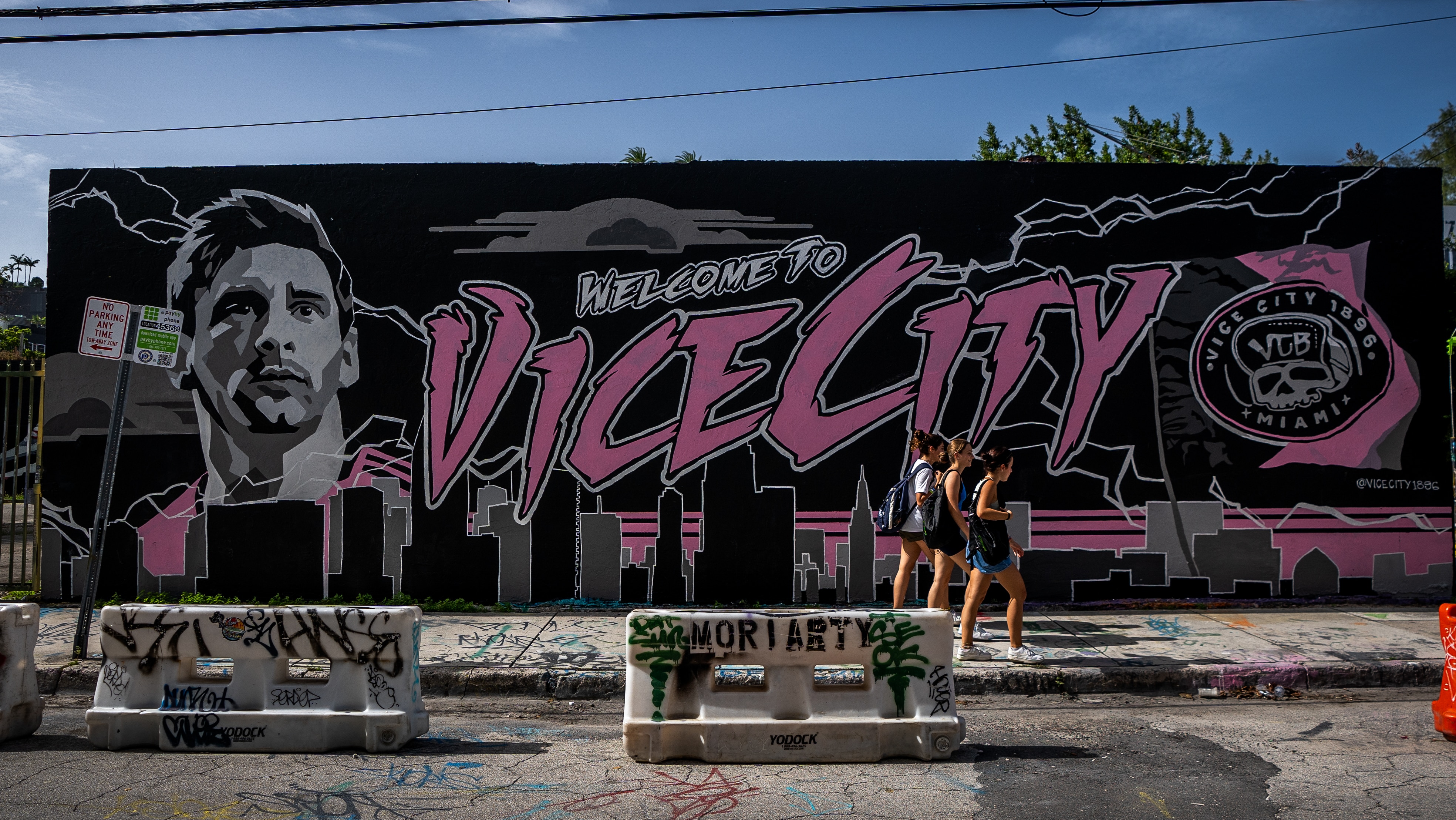 Two women walk past a mural that says WELCOME TO VICE CITY with a portrait of Lionel Messi
