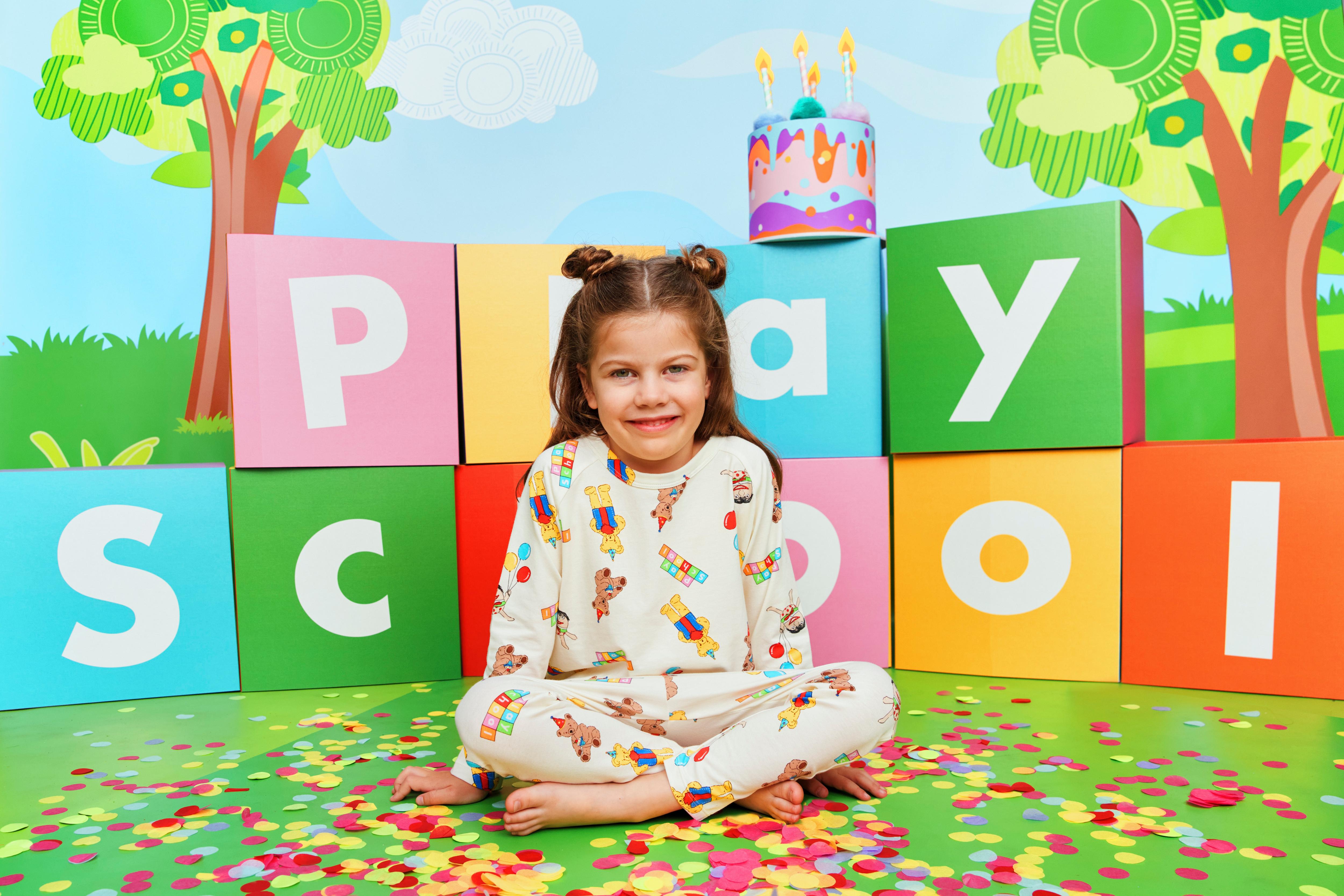 Child wearing Play School apparel sitting in front of colourful blocks reading 'Play School'