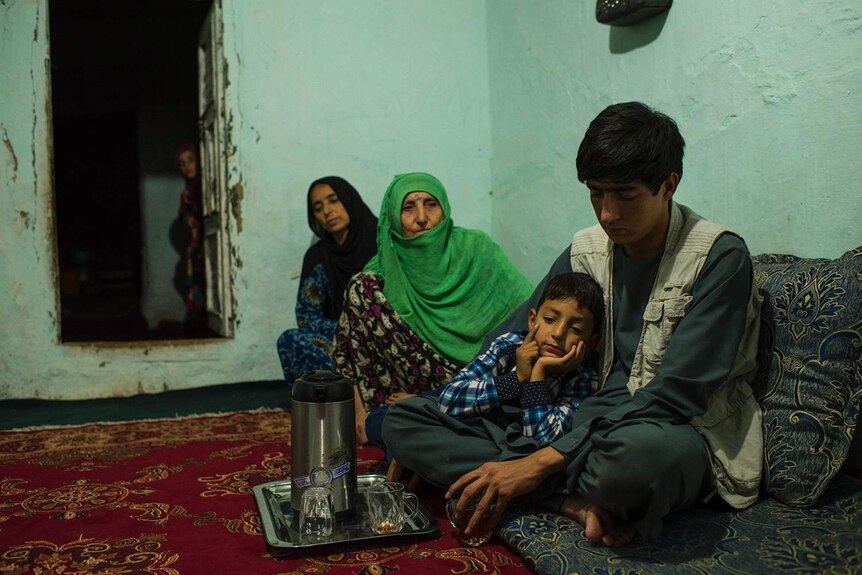A Kunduz family sit in a run-down green room at a tea set.