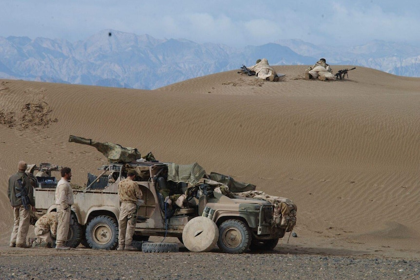 Sentries keep watch as soldiers change the tyres of a vehicle