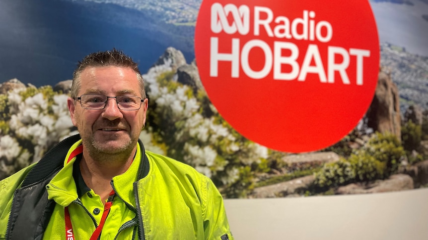 Man in work gear standing in front of ABC Radio Hobart sign.