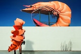 A photograph of a person in prawn costume looking at a giant prawn