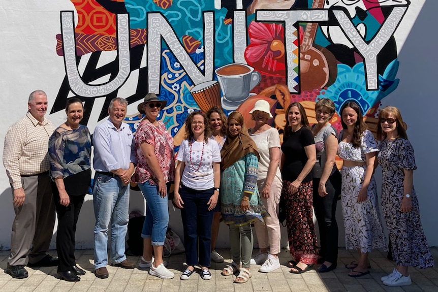 A group of 12 people standing in front of the Unity mural in the City of Canning, WA.