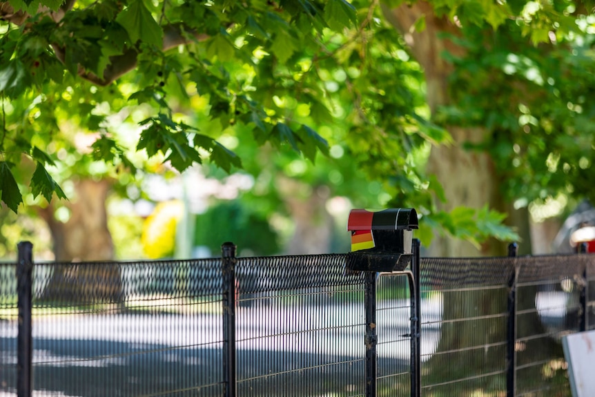 Coloured stickers on a black letterbox on a black metal fence in a tree-lined Sydney street.