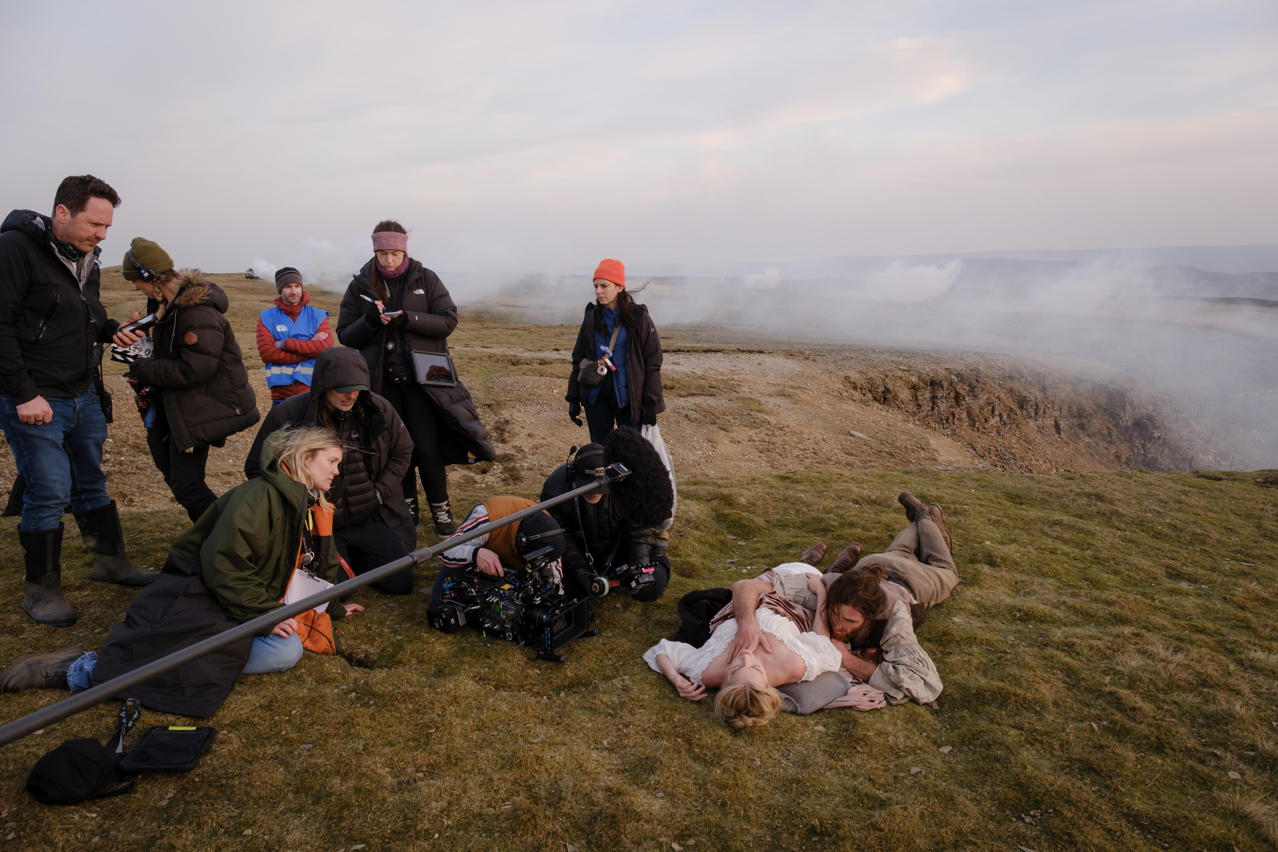 Dos personas yacían en una montaña cubierta de hierba rodeadas por un equipo de filmación.