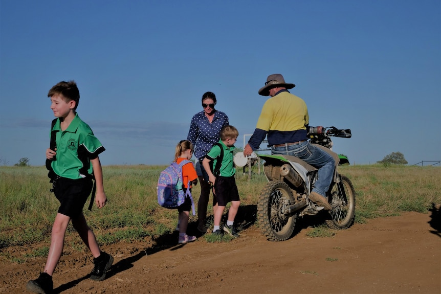 Parents on a motorbike say goodbye to their three children as they walk down a dirt road.