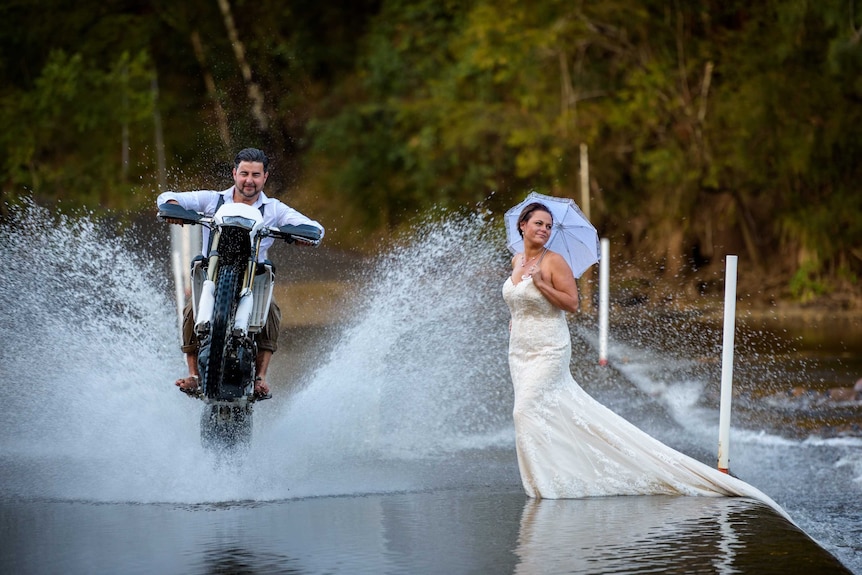 man doing wheelie on dirt bike and splashing woman with water