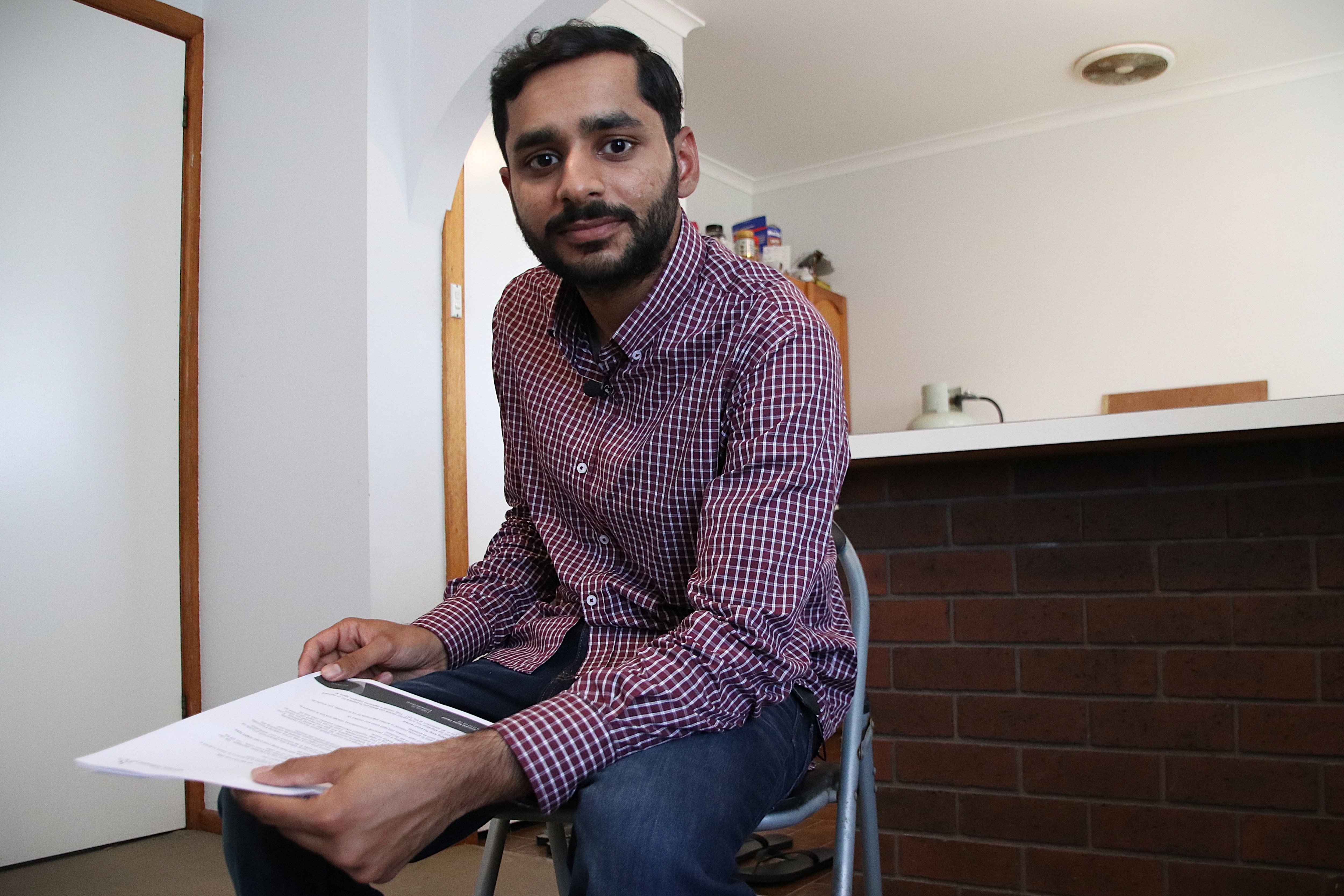 Miftah Ud Din sits near his kitchen, holding a printed letter.