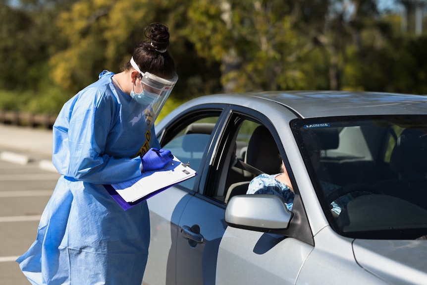 Un agent de santé écrit sur des papiers avec un automobiliste sur un site de test COVID à Brisbane