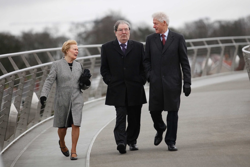 A woman wearing a coat walks along a bridge with two men.