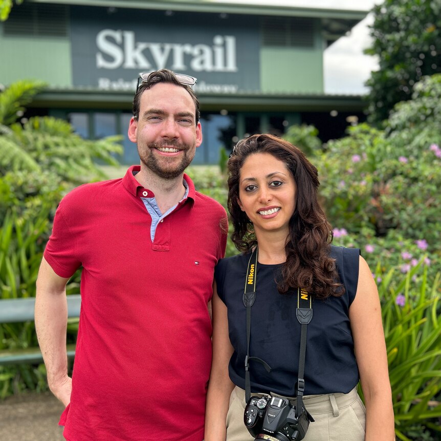 A young man and woman pose for a photo infront of some bushes